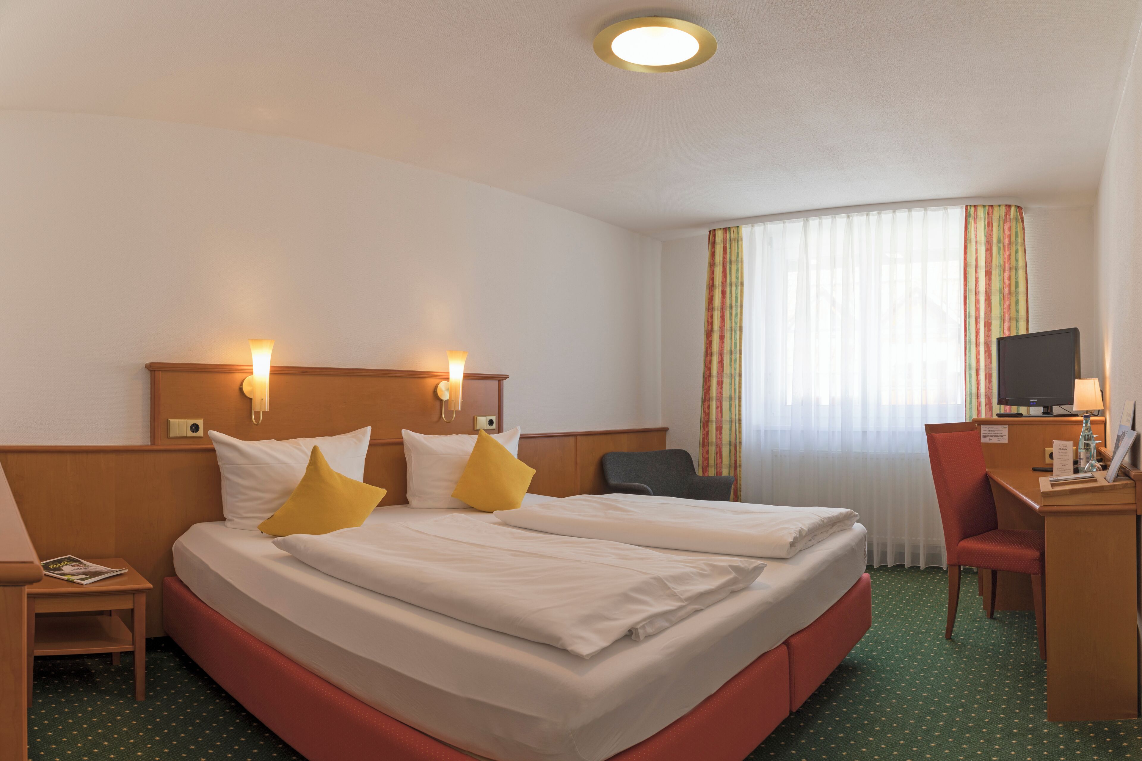 A hotel room with two beds, a desk, a chair, a TV, and a window with curtains.