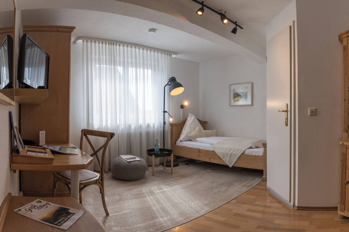 A bedroom with a bed, a desk, a chair, a lamp, and a window with curtains.