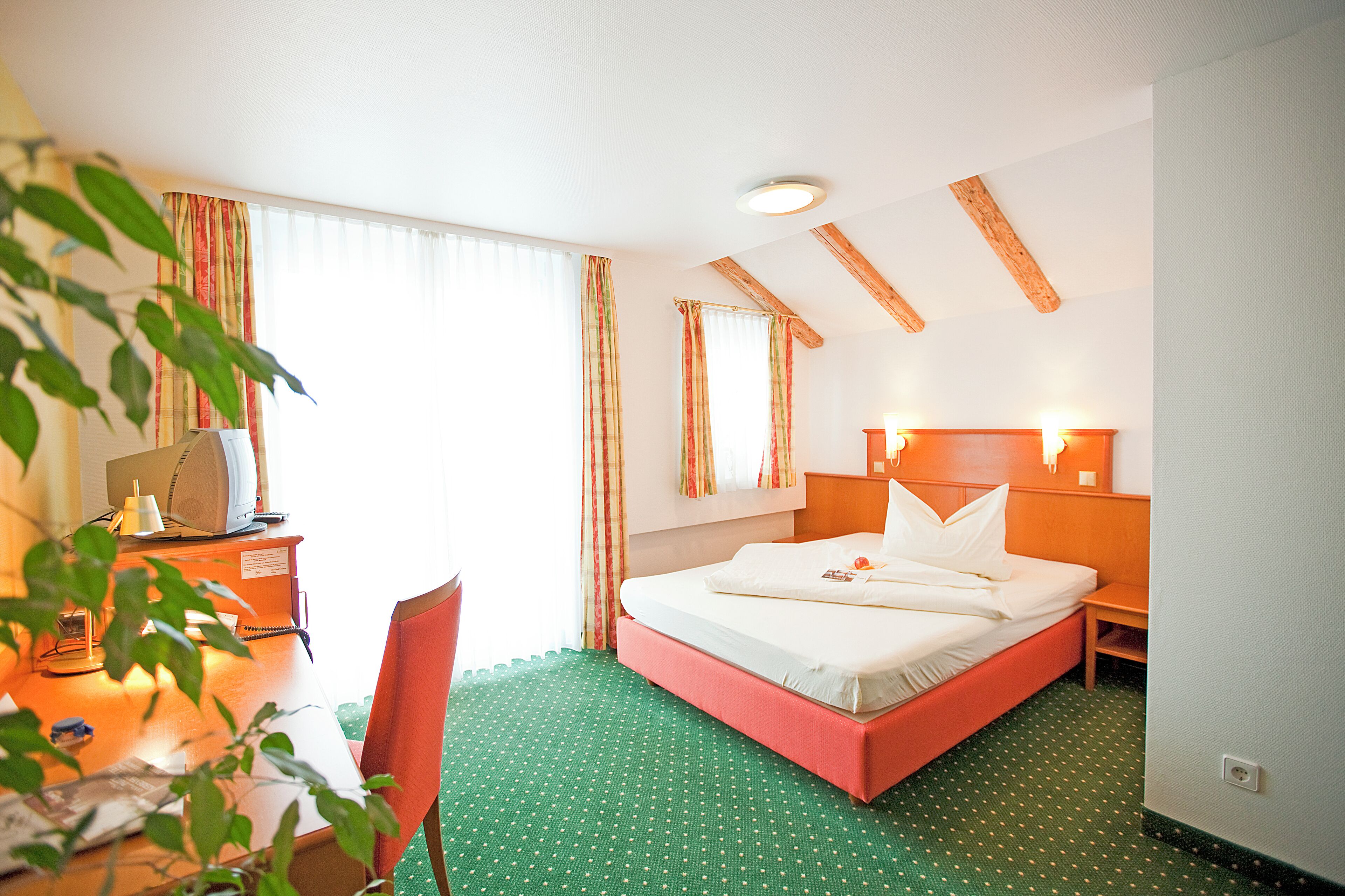 A hotel room with a bed, desk, chair, and a window with curtains.