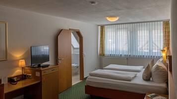 A hotel room with a bed, a desk with a lamp, a television, and a window with curtains.
