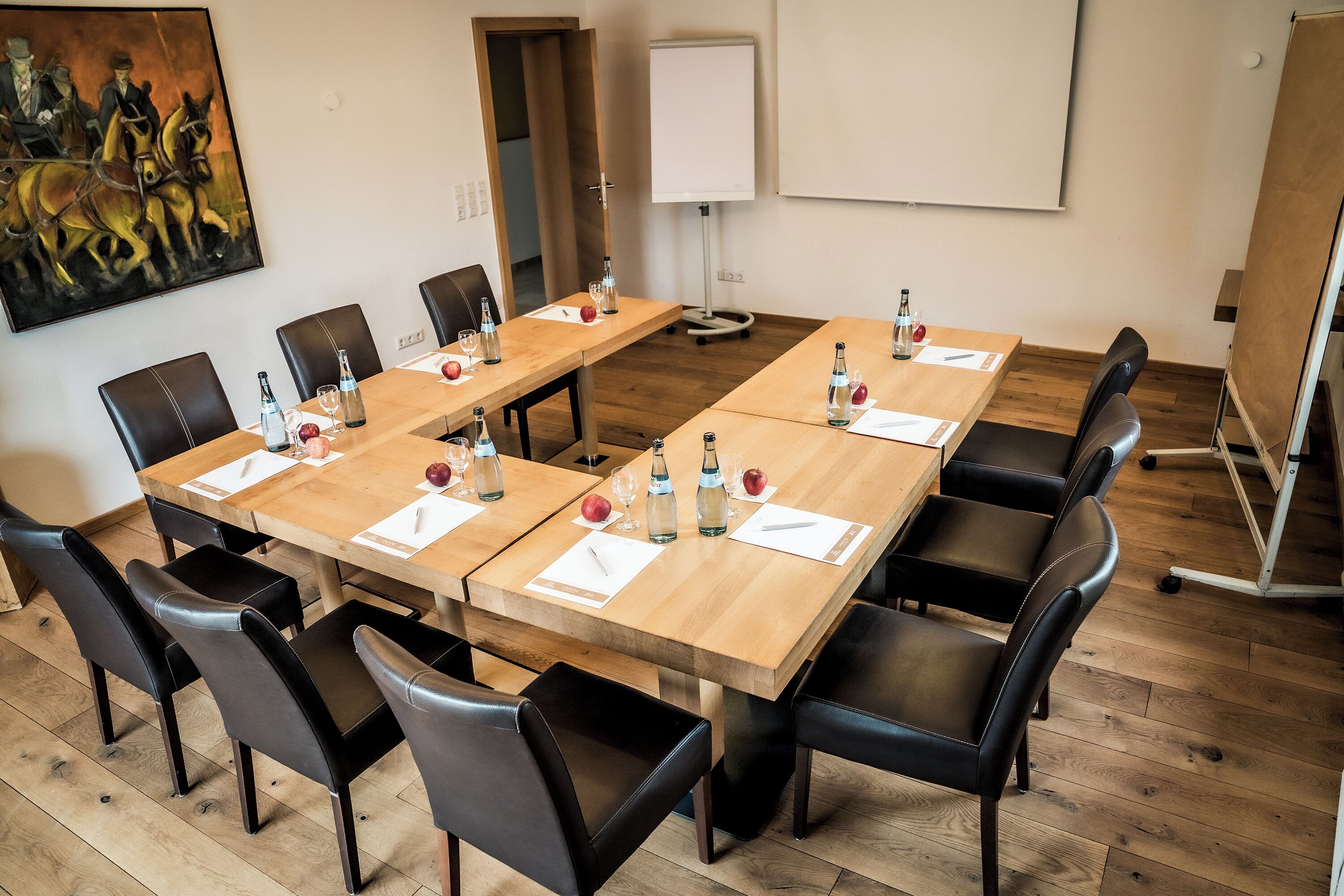 Une salle de conférence avec une longue table, des fauteuils en cuir noir et un tableau blanc.