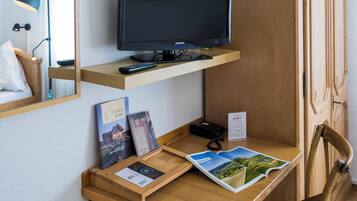Een hotelkamer met een houten bureau, een televisie, een stoel, een spiegel en een kast.