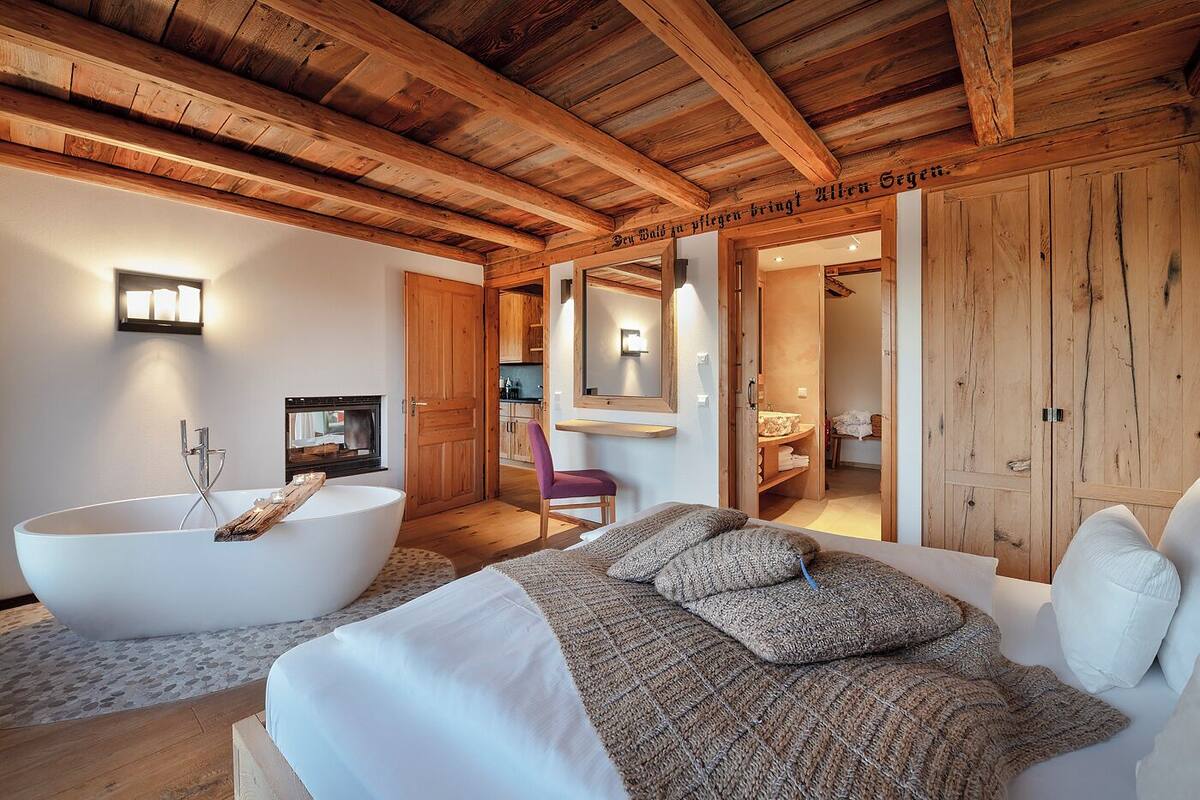 A modern bedroom with a large bathtub, a bed with a knitted blanket, and wooden walls.