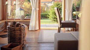 A cozy cabin interior with a wooden ceiling, a large window with curtains, a wicker basket, a cushioned bench, and a hanging pendant light.