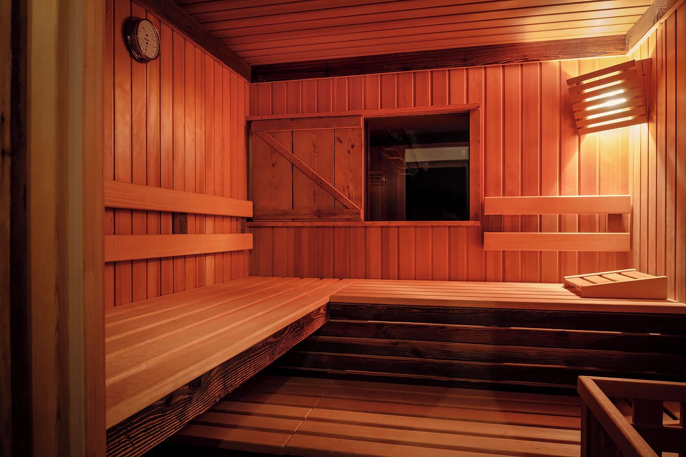 A wooden sauna with a bench, a window, and a clock on the wall.