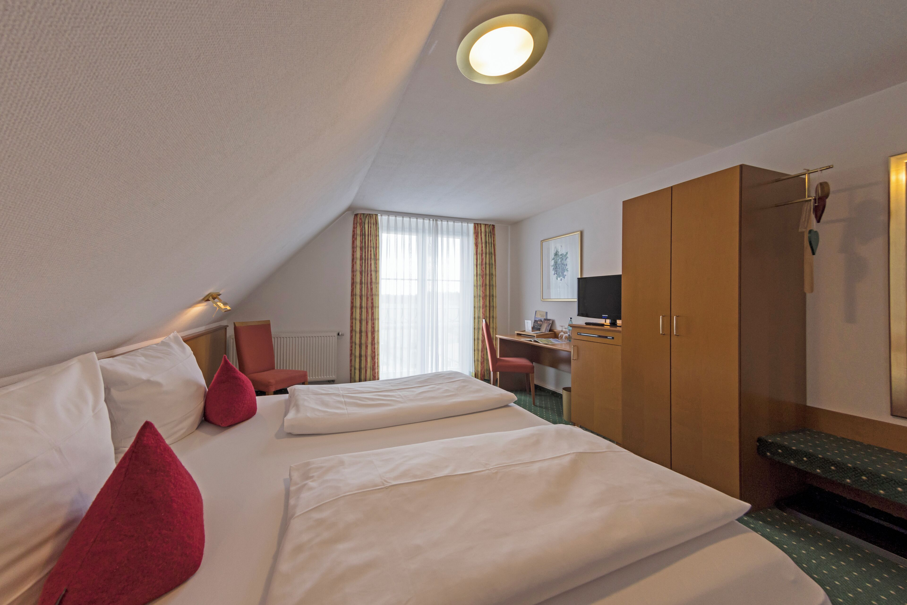 A hotel room with a bed, a desk, a chair, and a wardrobe.