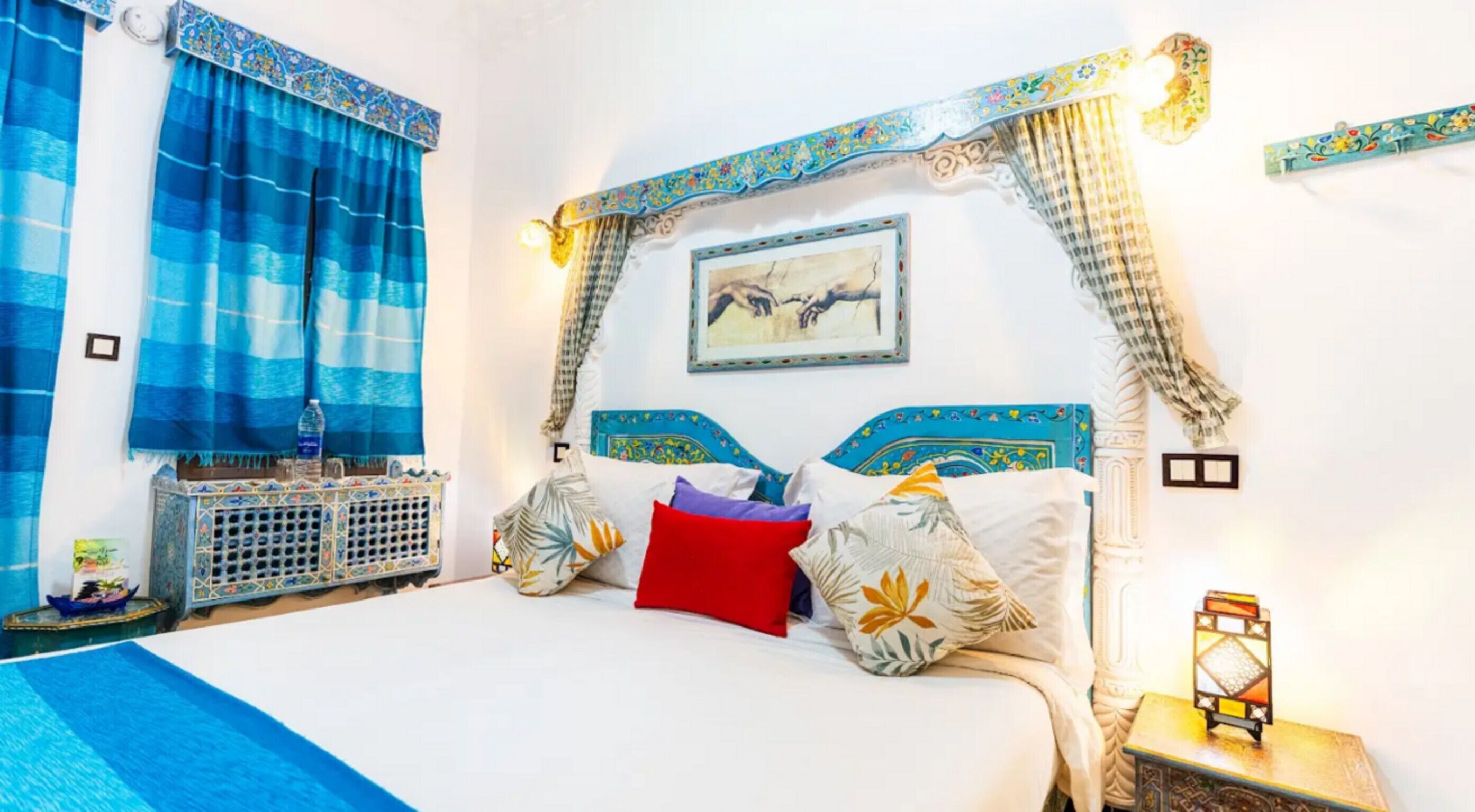 A bed with patterned pillows, a nightstand with a lantern, and a wall-mounted picture.