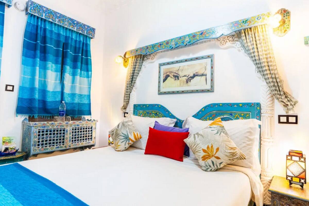 A bed with patterned pillows, a nightstand with a lantern, and a wall-mounted picture.