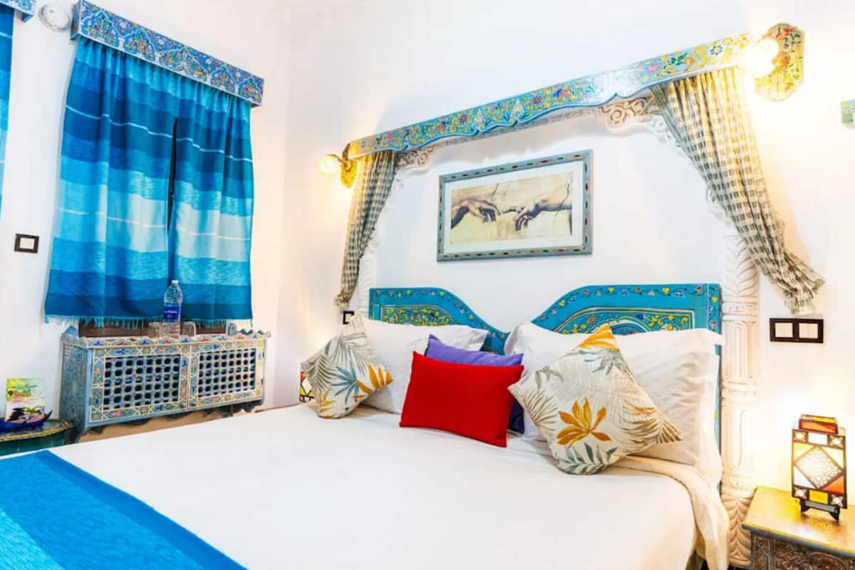 A bed with patterned pillows, a nightstand with a lantern, and a wall-mounted picture.