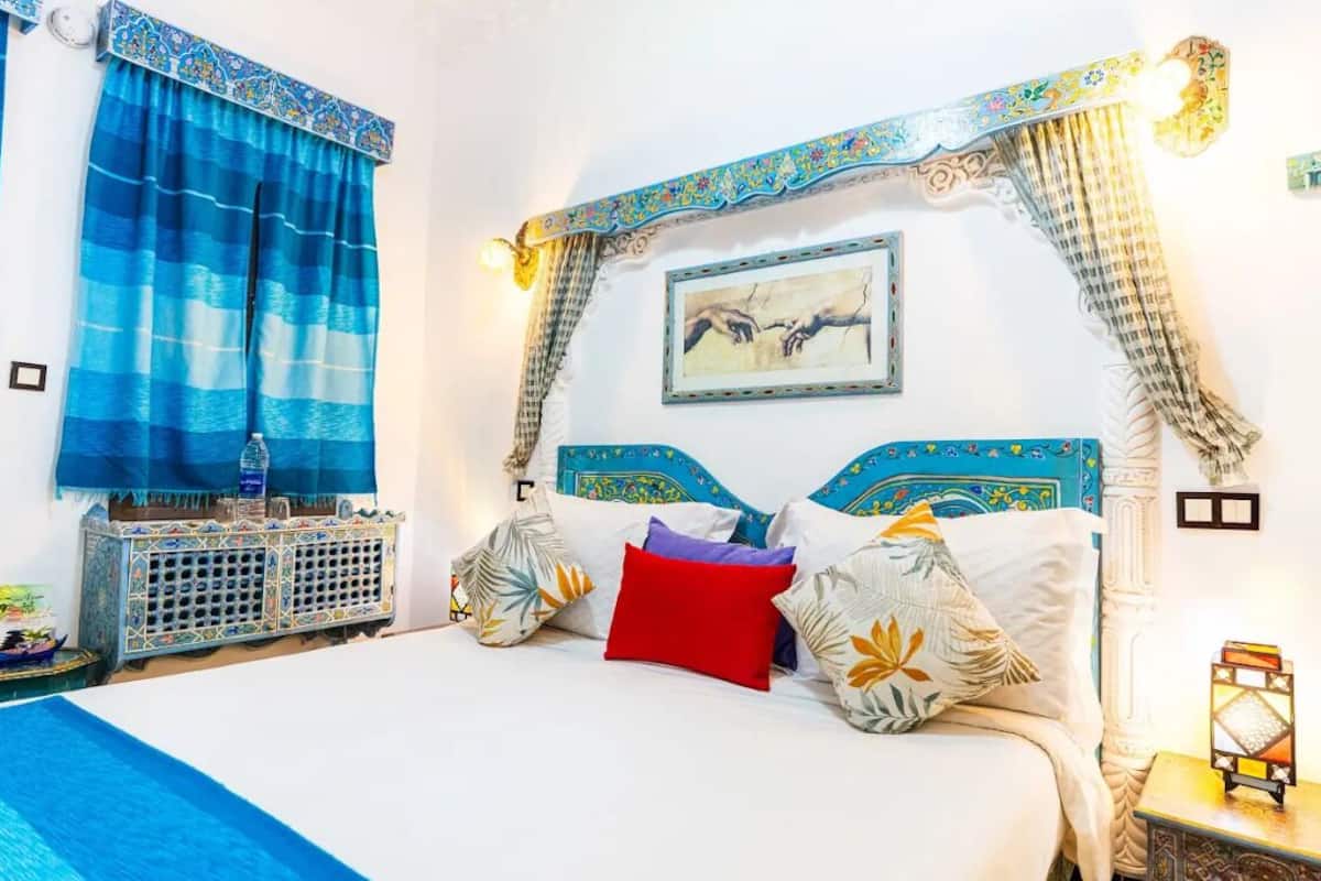 A bedroom with a bed, curtains, a nightstand, a wall-mounted picture, and a decorative headboard.