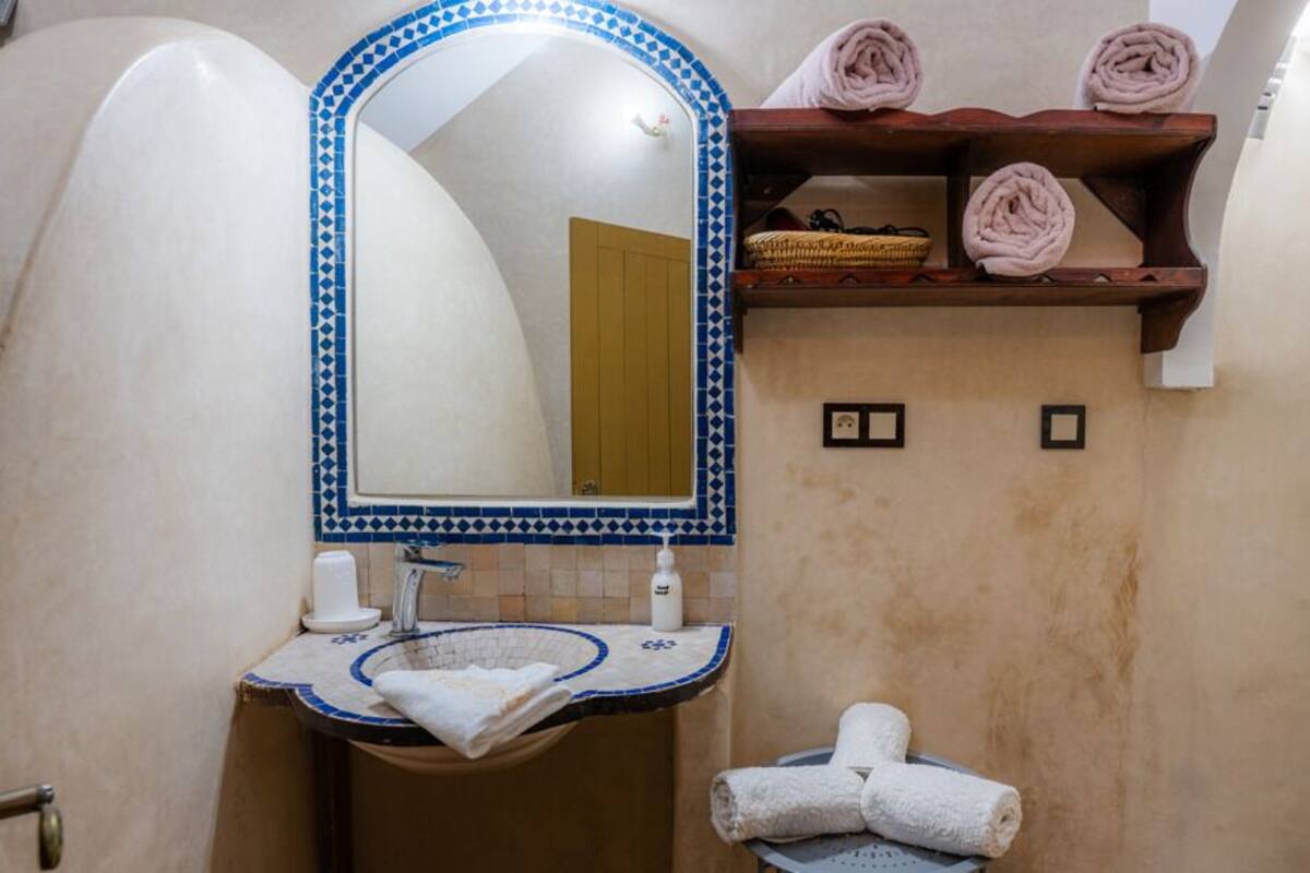 A bathroom with a sink, mirror, towel rack, and a wooden shelf with towels.