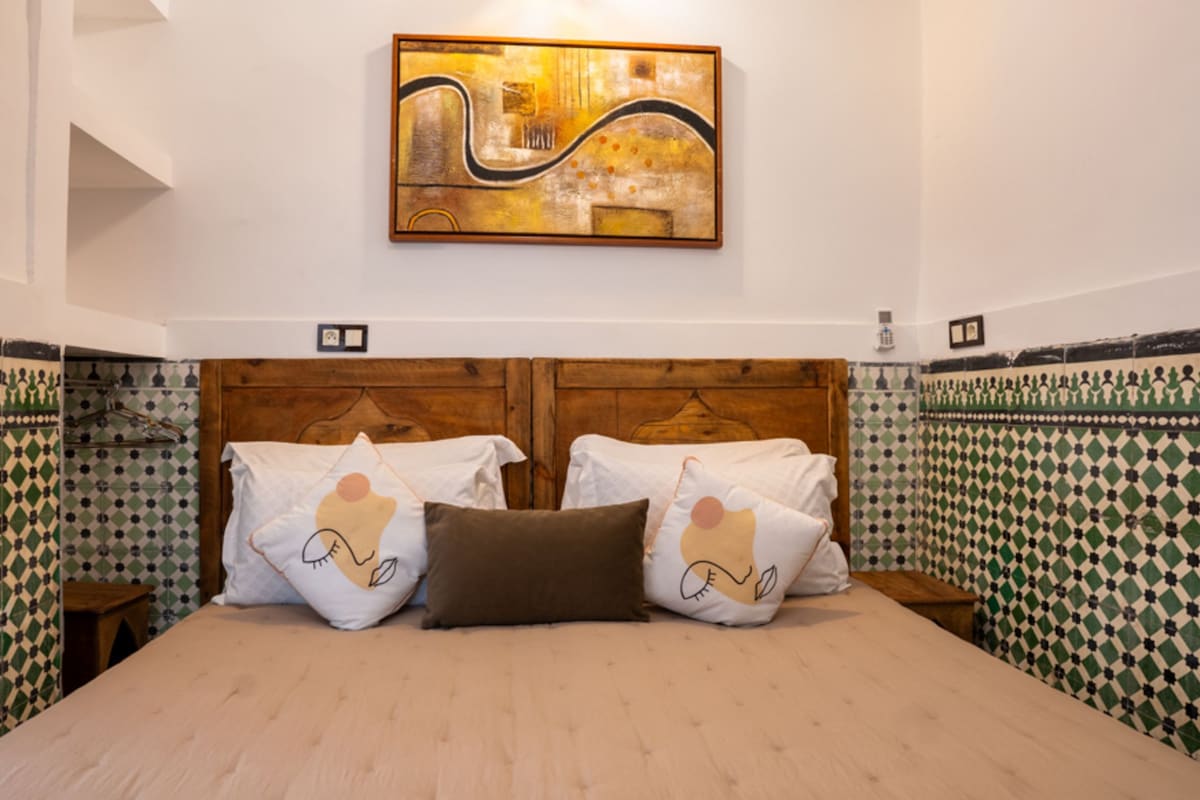 A hotel room with a wooden headboard, patterned walls, and a painting above the bed.