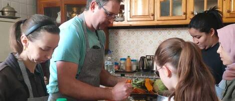 A group of people preparing food in a kitchen with wooden cabinets and a tiled backsplash.