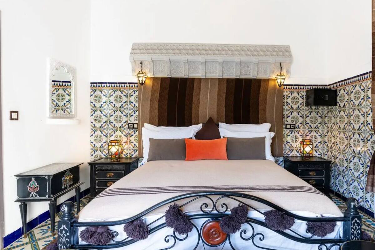 A bedroom with a large bed, two bedside tables, patterned walls, and a decorative ceiling.