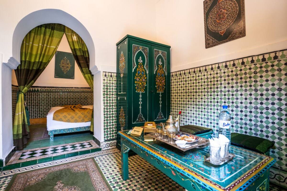 A room with a bed, a green cabinet, a table with items, and patterned walls.