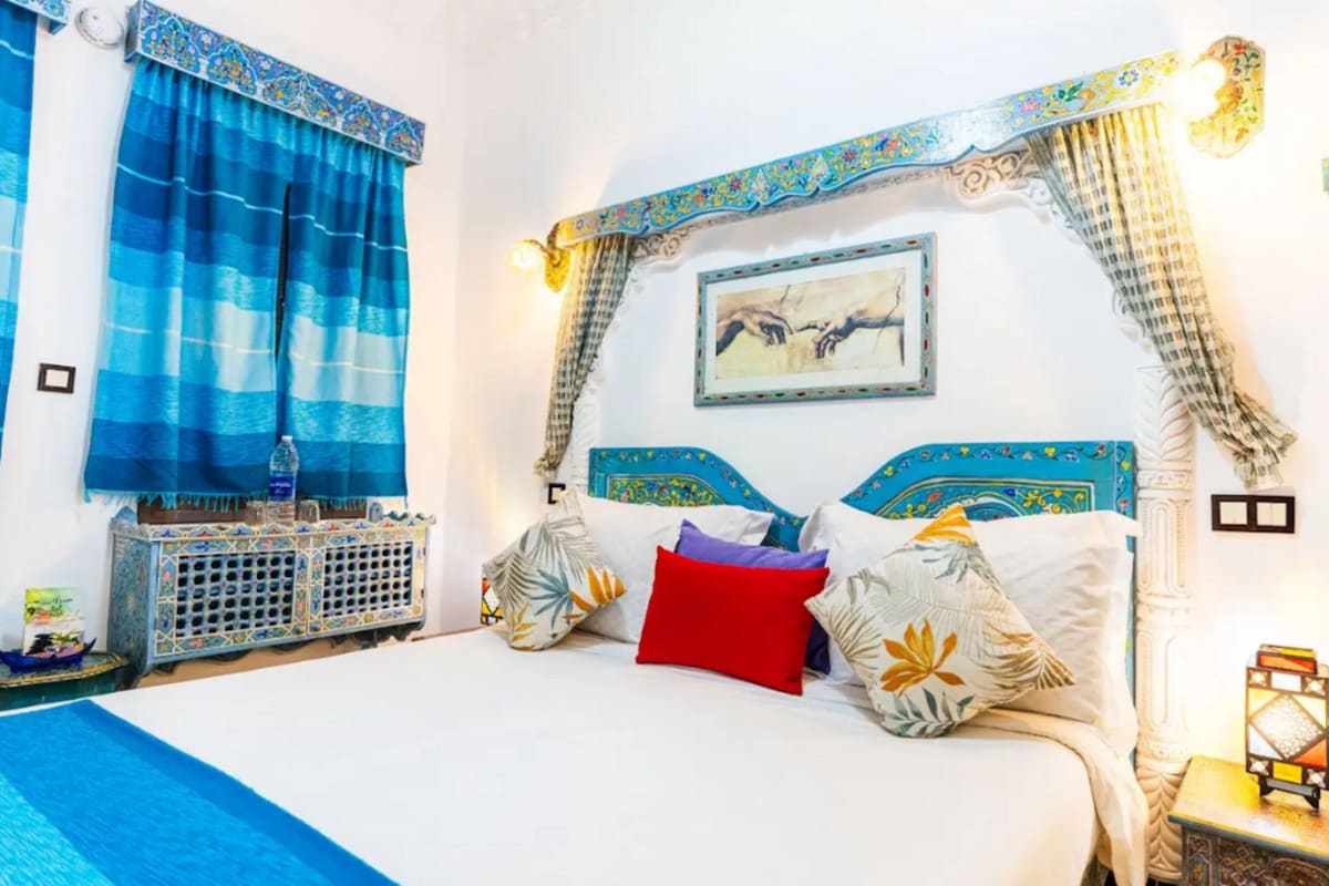 A bed with patterned pillows, a nightstand with a lantern, and a wall-mounted picture.