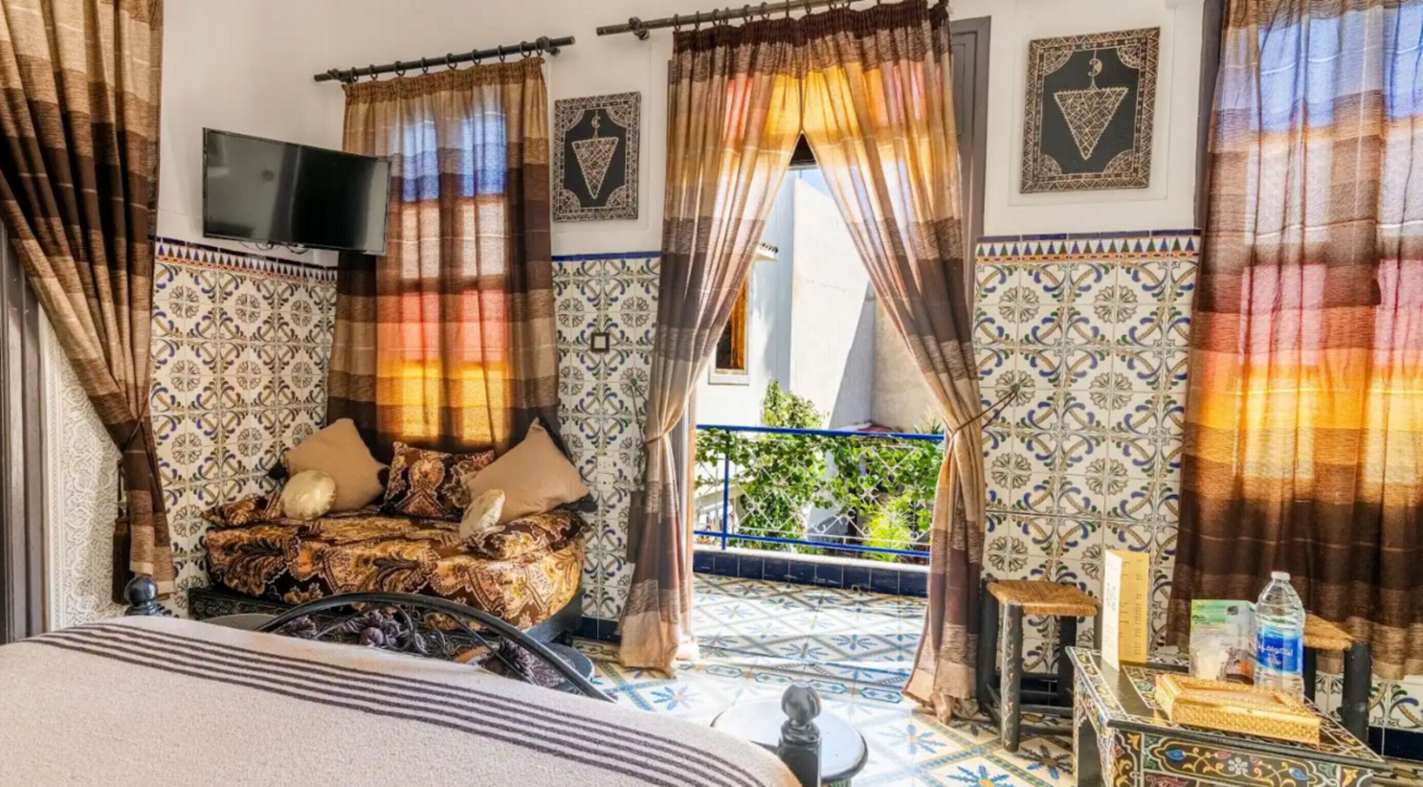A room with a bed, curtains, a TV, and a view of a balcony.