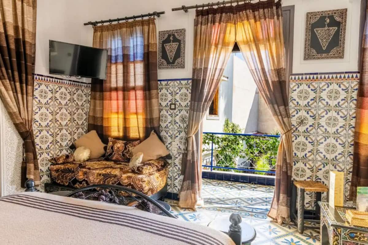 A room with a bed, curtains, a TV, and a view of a balcony.