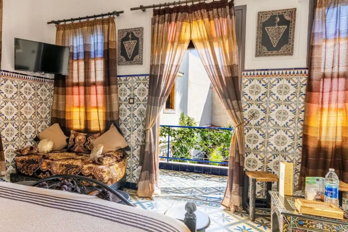 A room with a bed, curtains, a TV, and a view of a balcony.