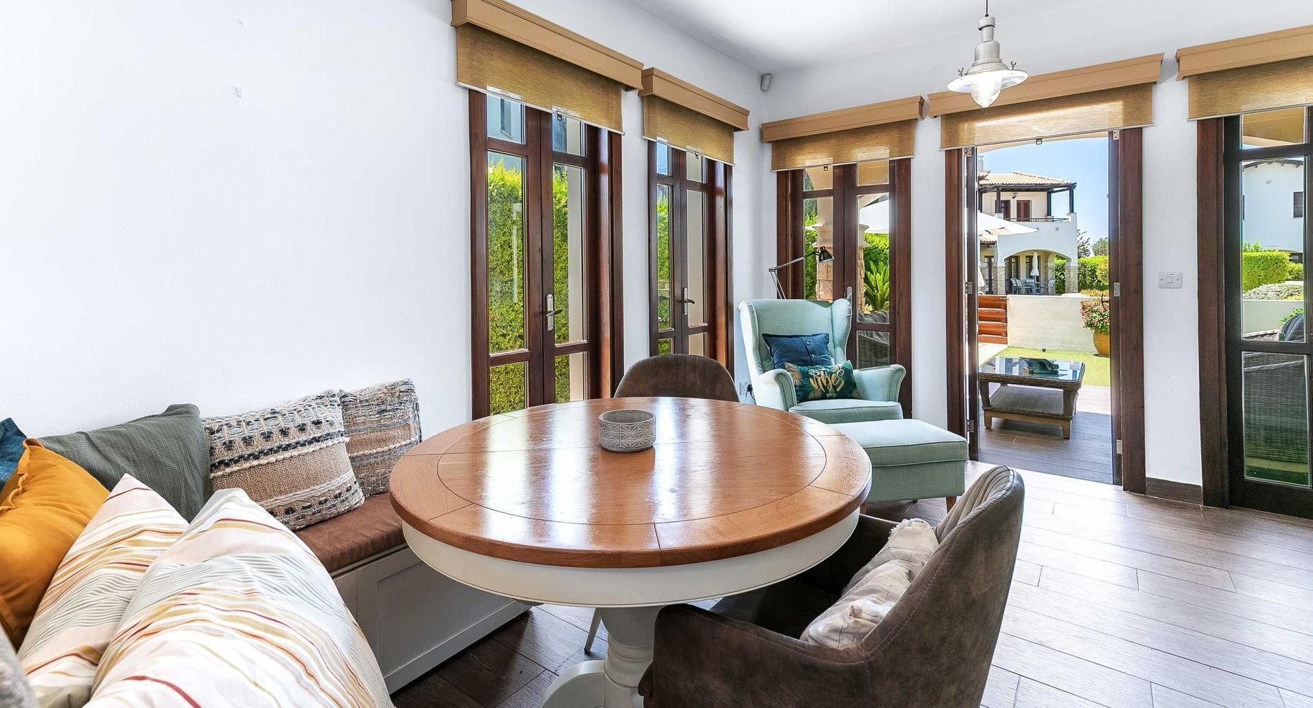 Una sala moderna con una mesa redonda de madera, un sofá y una silla. Amplias ventanas ofrecen vistas al exterior.