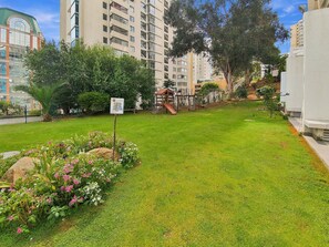 A well-maintained grassy area with a playground, surrounded by residential buildings and trees. - Oceana Suites Alto Libertad (Vina del Mar)