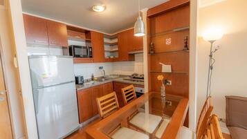 Una cocina compacta con armarios de madera, un refrigerador, un microondas y una mesa de comedor con sillas.