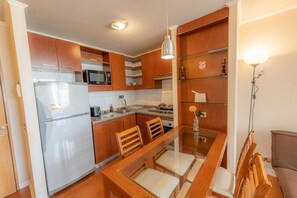 Une cuisine compacte dotée de meubles en bois, d’un réfrigérateur, d’un four à micro-ondes et d’une table à manger avec des chaises.