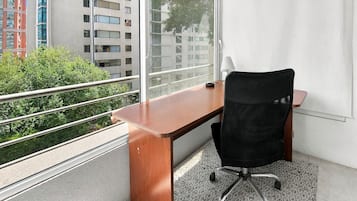 Espacio de oficina moderno con escritorio de madera, silla de oficina negra y un gran ventanal con vistas a edificios y áreas verdes.