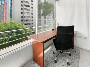 Un espace de bureau moderne avec un bureau en bois, un fauteuil de bureau noir et une grande fenêtre donnant sur des bâtiments et des espaces verts.