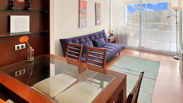Un salon moderne avec une table à manger en verre, un canapé et une grande fenêtre donnant sur la ville.