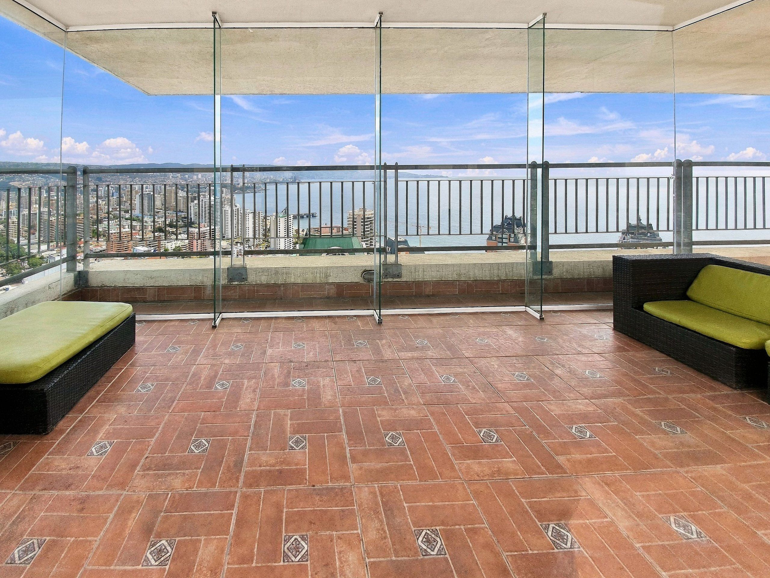 Ein Balkon mit Fliesenboden, Glasgeländern und zwei Korbsesseln mit Kissen.