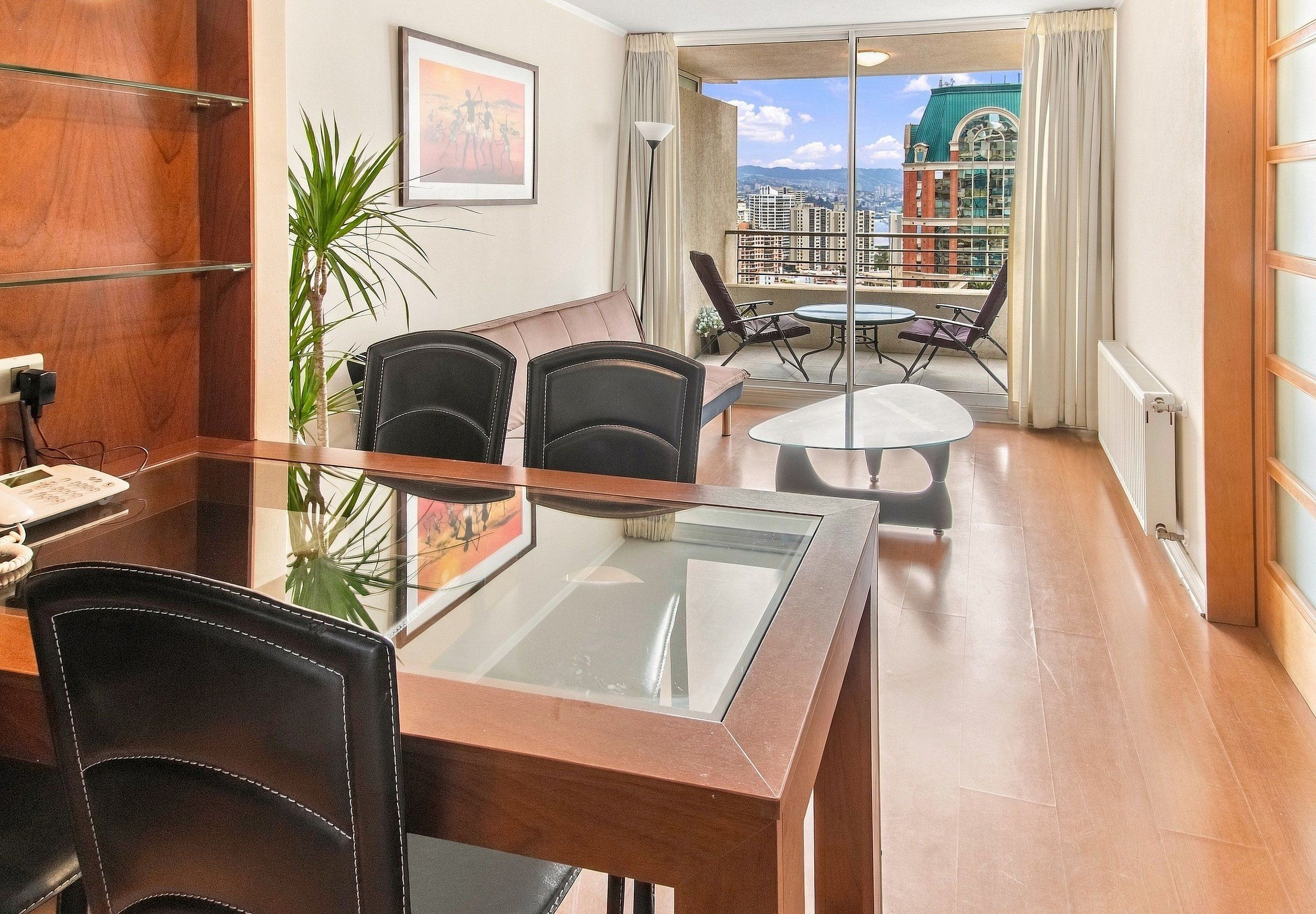 Ein modernes Hotelzimmer mit Essbereich, einem Balkon und Blick auf die Stadt sowie einem großen Fenster.