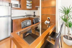 A modern kitchen with wooden cabinets, a microwave, and a dining area with a glass table and chairs.
