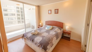 Ein Schlafzimmer mit einem gro ßen Fenster, einem Bett mit einem gemusterten Überwurf, zwei Nachttischen mit Lampen und einer Wand mit zwei gerahmten Bildern.