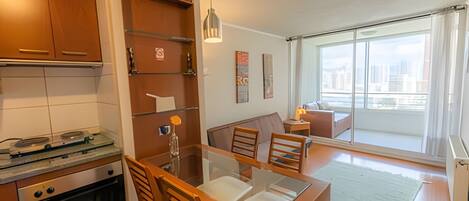 Una cocina moderna con armarios de madera, una mesa de comedor con sillas, un sofá y un ventanal con vistas a la ciudad.