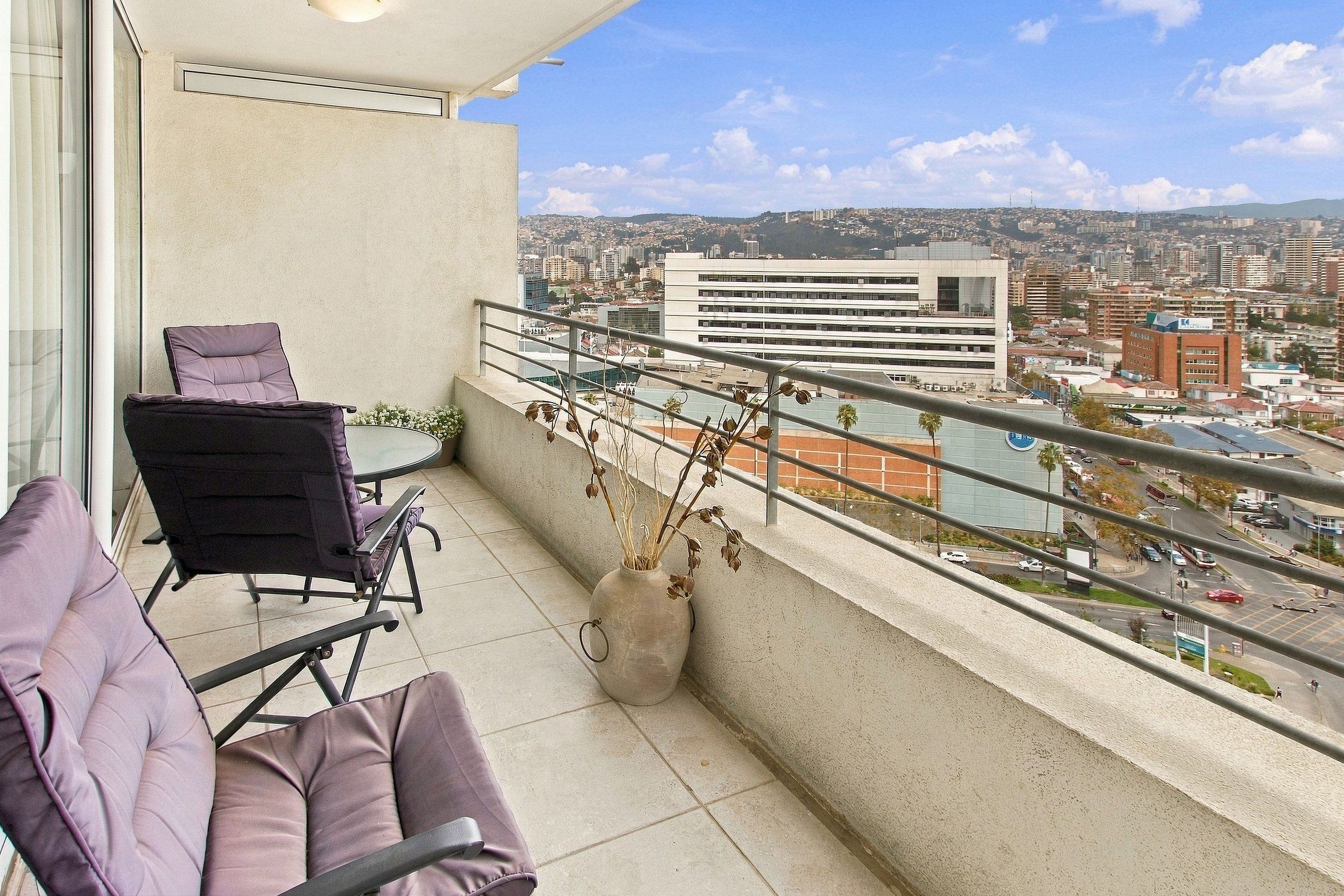 A balcony with a view of a cityscape, a chair, and a vase with dried plants.