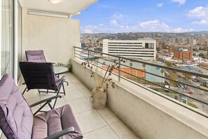 A balcony with a view of a cityscape, a chair, and a vase with dried plants. - Oceana Suites Alto Libertad (Vina del Mar)