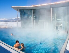 Ein Thermalbecken mit Glasumrandung, umgeben von Schnee und Bergen.