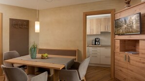 A modern kitchen with wooden cabinets, a dining area with a table and chairs, and a television mounted on the wall. - Traum-ferienwohnung mit Dachterrasse & Tollem Ausblick, Cron4 Schwimmbad & Sauna (Brunico)