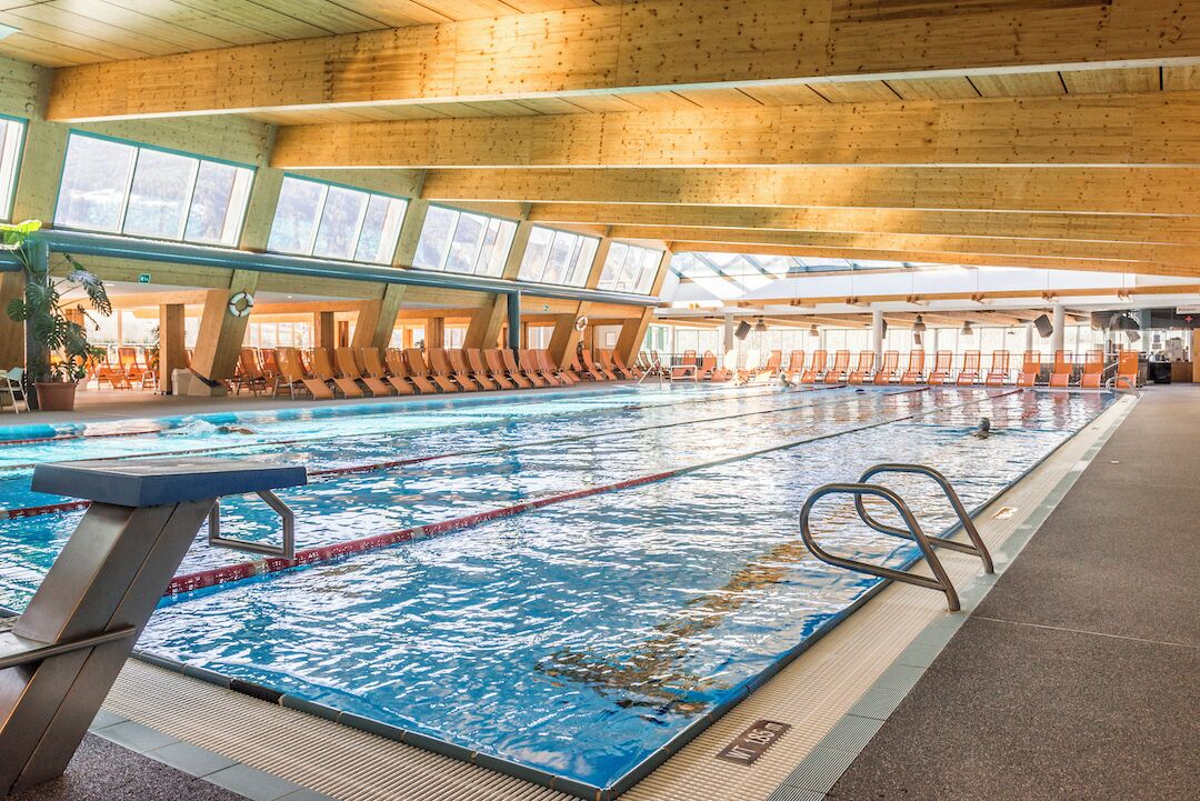 Una piscina interior amb bigues de sostre de fusta, línies de separació netes i finestres que deixen passar la llum del sol.