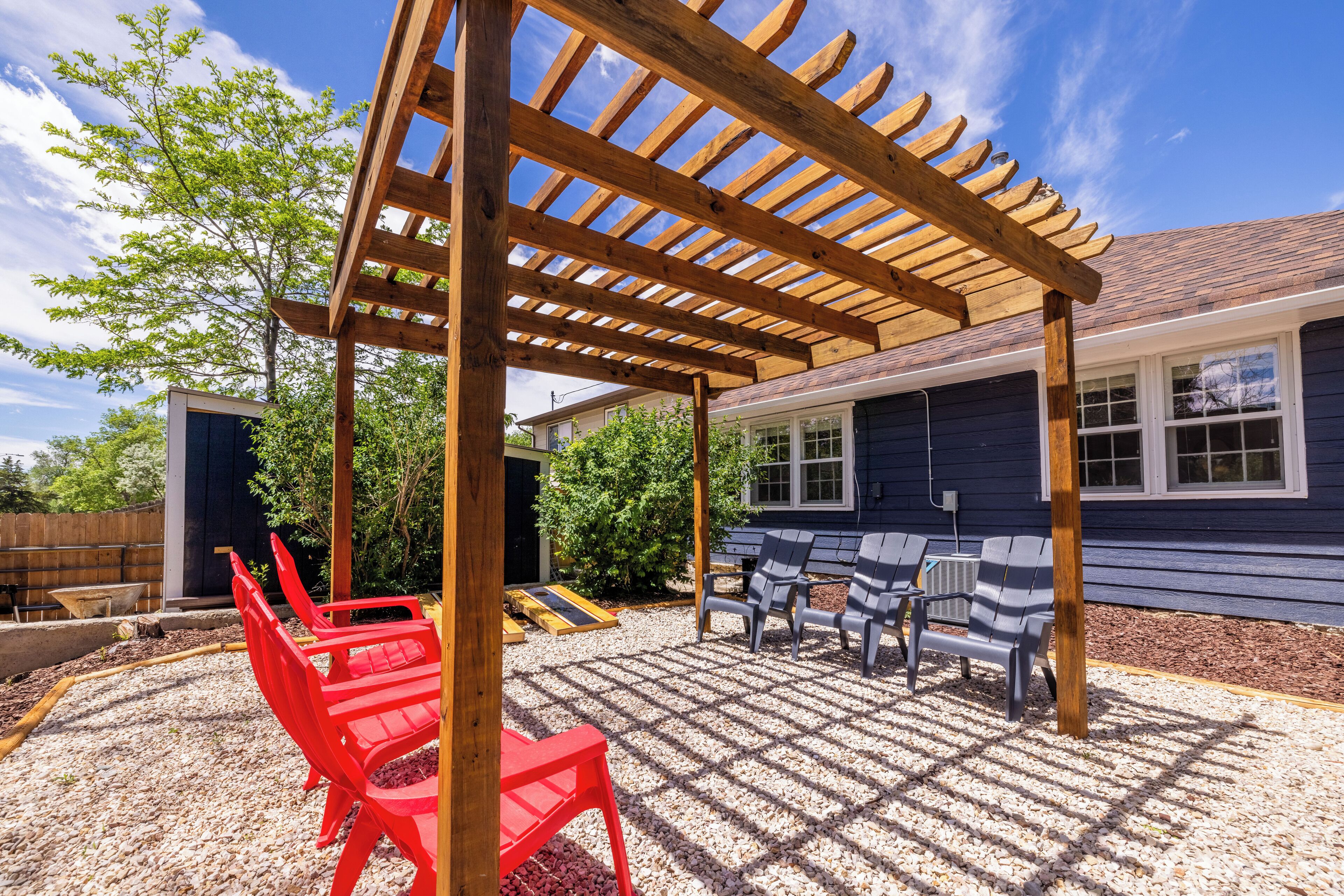 A covered patio with a pergola, outdoor seating, and a house in the background.