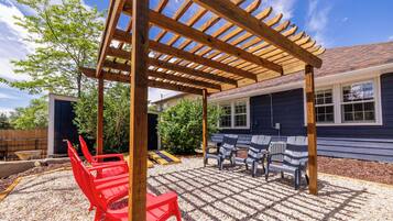 A covered patio with a pergola, outdoor seating, and a house in the background.