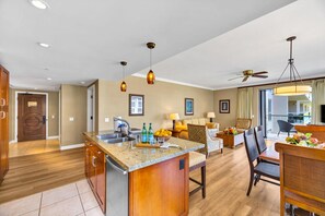 A spacious kitchen with a central island, a dining area with a table and chairs, and a living room with a sofa and a TV.