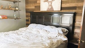 A bedroom with a wooden headboard, a bed with white bedding, a shelf with decorative items, and a painting of a deer. - House for Rent- EAA  (Oshkosh)