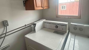 A compact laundry room with a front-loading washer and dryer, wooden cabinets above, and a window providing natural light. - Clean & Quiet Studio Apartment B (Nome)