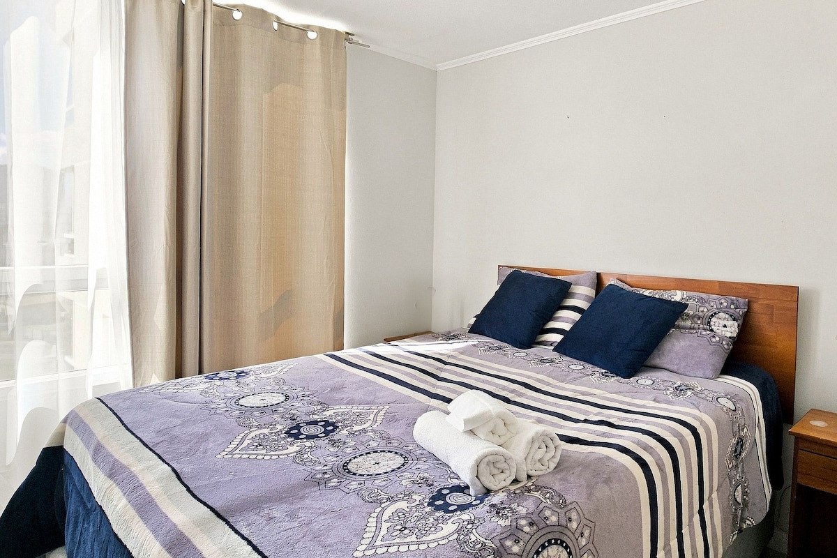 Une chambre d’hôtel avec un lit, une table de chevet, une lampe et une fenêtre avec des rideaux.