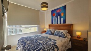 Ein Schlafzimmer mit einem großen Bett, einem hölzernen Kopfteil, Nachttischlampen, einem Fenster mit Blick und einem Bild an der Wand.