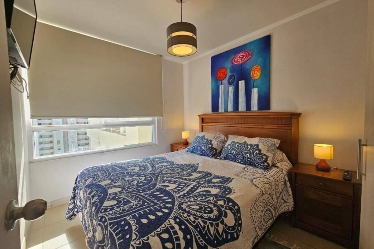 Quarto com uma cama grande, cabeceira de madeira, abajures, janela com vista e um quadro na parede.