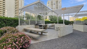 Ein Außenbereich mit Terrassengestaltung, einer Pergola, Sitzgelegenheiten und einem Blumenbeet.