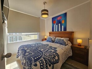 Une chambre à coucher avec un grand lit, une tête de lit en bois, des lampes de chevet, une fenêtre donnant sur un beau paysage et un tableau accroché au mur.